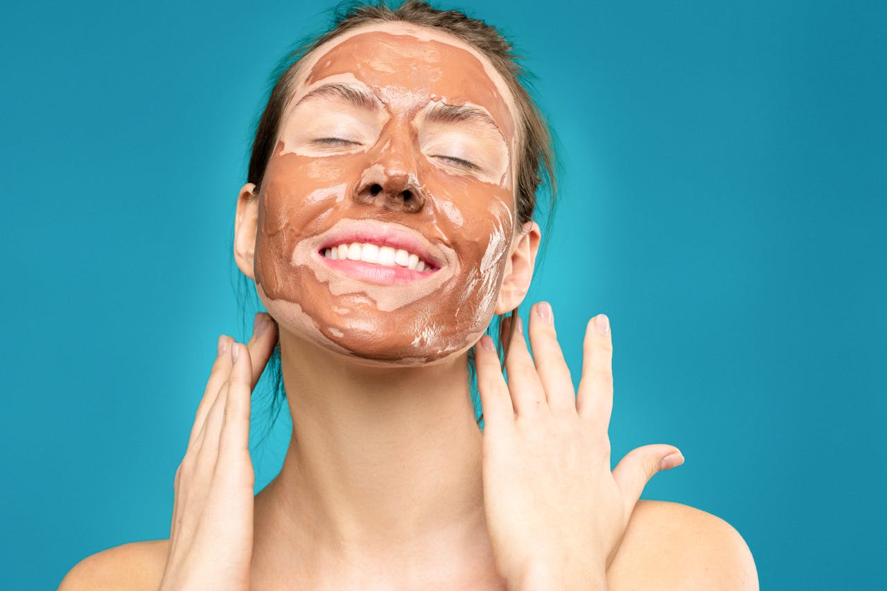 creative-01 Close-up of a smiling woman with a clay facial mask, conveying relaxation and skincare routine.